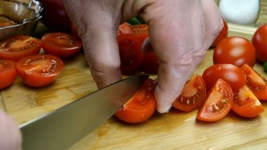 Şefin elleri lezzetli yemekler hazırlamak için kiraz domatesini ahşap kesme tahtasıyla keskin mutfak bıçağıyla parçalara ayırdı. Ev mutfağı. Yakın plan..