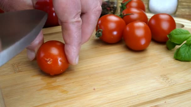 Las manos del chef cortan el tomate cherry en trozos con un cuchillo de cocina afilado en una tabla de cortar de madera para preparar deliciosa comida. Cocina casera. Primer plano. — Vídeos de Stock