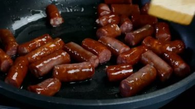 Lezzetli yağlı sosisler, parçalara ayrılmış, sebze yağında kızartma tavasında kızartılıyor. Hızlı besleyici yiyecekler. Ev mutfağı. Yakın plan..