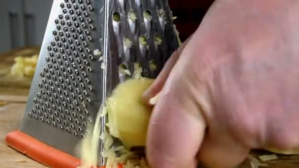 Cook rub raw potatoes with his hands on metal kitchen grater for vegetarian food cooking. Fast movements. Domestic kitchen. Close-up. — Stock Video