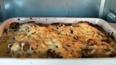 Etin üzerinde sebzelerle eritilen peynir, fırında kızartılır. Ev mutfağı. Titrek hafif, ağır çekim. Yakın plan..