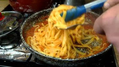 Lezzetli domates sosuyla sebzeleri karıştırılmış spagetti. Gaz sobasında tavada kaynatılmış. Ev mutfağında makarna ya da tagliatelle tarifi. Yakın plan..