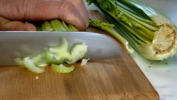 Ręce szefa kuchni siekanie selera łodygi do małych plasterków z nożem kuchennym na drewnianej tablicy kuchennej do sałatki warzywnej. Świeży zdrowy seler do jedzenia i gotowania. Śródziemnomorska dieta. Zbliżenie. — Wideo stockowe