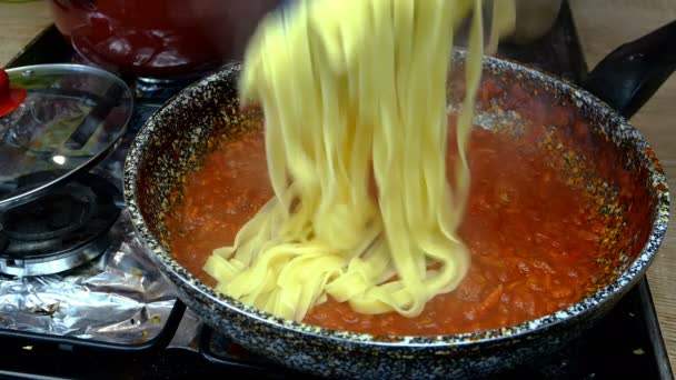 Spaghetti in pikante Tomatensauce mit Gemüse geben, in der Pfanne auf Gasherd köcheln lassen. Rezept zur Zubereitung von Pasta oder Tagliatelle in der heimischen Küche. Nahaufnahme. — Stockvideo