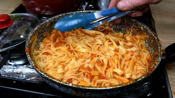 Spaghetti mixing with savory tomato sauce with vegetables, simmer in frying pan on gas stove. Recipe for making pasta or tagliatelle in home kitchen. Close-up. — Stock Video