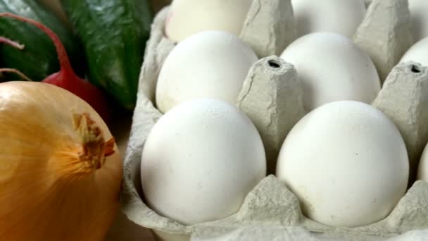 White chicken eggs are fresh, stacked in ecological cardboard packaging and fresh vegetables. Food background. Selective focus. Close-up. — Stock Video