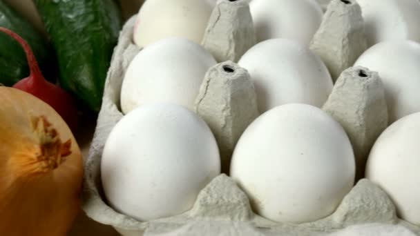 Bílá kuřecí vejce jsou čerstvá, navršená v ekologických lepenkových obalech a čerstvé zelenině. Pozadí jídla. Selektivní soustředění. Detailní záběr. — Stock video