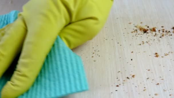 Tangan manusia dengan sarung tangan karet kuning dengan kain biru dengan microfiber, dengan hati-hati membersihkan meja dari remah-remah roti. Disinfeksi, pekerjaan rumah tangga, konsep sanitasi. Close-up. — Stok Video