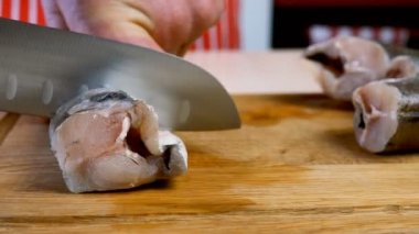 Aşçı hake leşini veya pollock balığını lezzetli yemekler hazırlamak için keskin bıçakla parçalara ayırır, yerli mutfağın tahta kesme tahtasıyla. Kızarmış balık tarifi. Seçici odak.