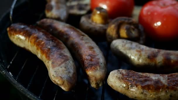 Faire frire les saucisses bavaroises grasses cuites sur un gril ou une grille de barbecue. Avec des légumes tomates et champignons. Gros plan. — Video