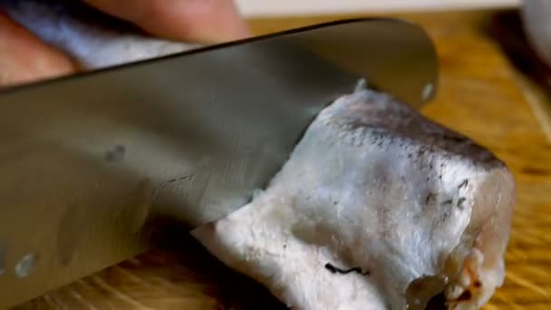 Cook corta la carcasa de merluza o pez abadejo en trozos con cuchillo afilado para preparar deliciosa comida, sobre tabla de cortar de madera en la cocina doméstica. Receta de pescado frito. Enfoque selectivo. — Vídeos de Stock