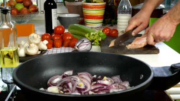 Table dans la cuisine domestique. Préparation de plats méditerranéens. Poêle à frire avec oignon tranché. Chef de coupe de viande de poulet pour faire une sauce savoureuse avec tomate, oignon, céleri, champignons. Gros plan. — Video