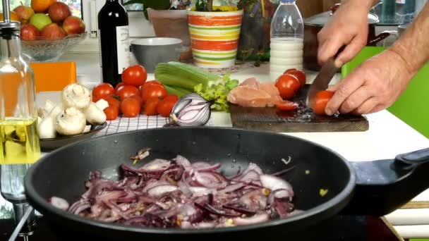 Tafel in de keuken. Voorbereiding van mediterraan voedsel. Braadpan met gesneden ui. Chef tomaat snijden voor het maken van smakelijke saus met kippenvlees, ui, selderij, champignons. Close-up. — Stockvideo