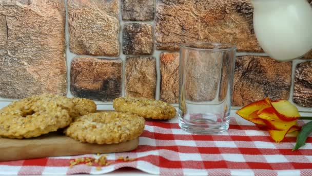 Färsk naturlig mjölk hälls i glas från flaska mot tegelvägg bakgrund på i bur servett. Fylla dricksglas med mjölk. Friska mejeriprodukter livsmedelskoncept. Närbild. — Stockvideo