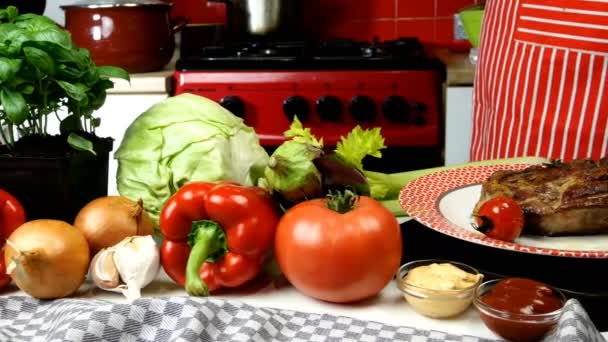 O chef decora a carne frita na chapa com tomates de cereja fritos e alecrim. Vários vegetais estão na mesa da cozinha para preparar um delicioso almoço saudável. Dolly atirou. Plano médio. — Vídeo de Stock