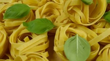 Bir sürü kuru tagliatelle makarnası, fesleğen yapraklarıyla süslenmiş, saat yönünün tersine daire şeklinde. Yakın plan..