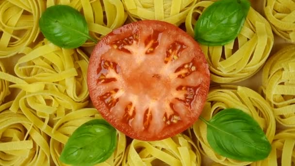 Veel droge tagliatelle pasta, versierd met basilicum bladeren en gesneden tomaat in het midden van de cirkel, draaien met de klok mee. Bovenaanzicht opname. Langzame beweging. Close-up. — Stockvideo