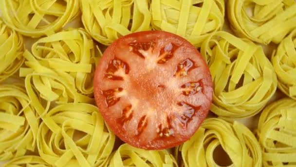 Lots of dry tagliatelle pasta, garnished with cut tomato in center of circle, rotate clockwise. Top view shot. Close-up. — Stock Video