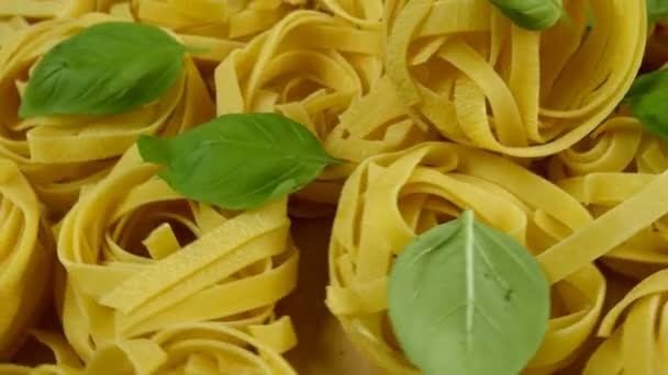 Massor av torr tagliatelle pasta, garnerad med basilika blad, rotera cirkel moturs. Närbild. — Stockvideo
