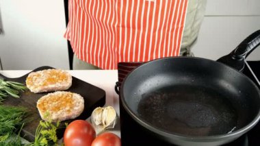 Şef mutfak masasındaki evcil mutfakta hamburger için tavuk pirzolası hazırlıyor. Sıcak tavaya kıyma, yağ ve biberiye filizleriyle garnitür koyuyor. Ortam planı.
