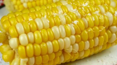 Üzerine tuz ve eritme yağı serpiştirilmiş tatlı mısır. Tuz taneleri sıcak mısır ve tereyağı yağının üzerine düşer. Yakın plan..