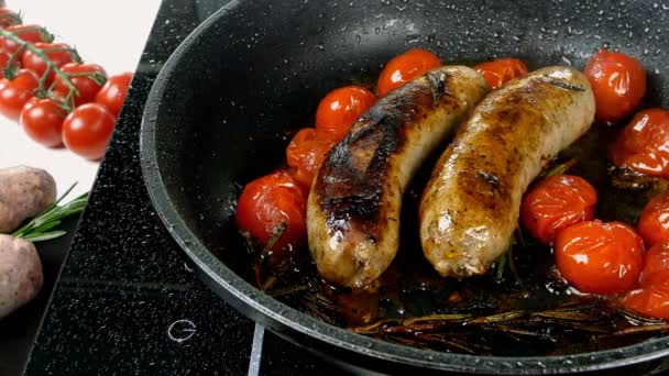 Les saucisses bavaroises blanches grasses avec tomate et brin de romarin sont frites dans une poêle sur une cuisinière électrique. Petit déjeuner anglais ou allemand, européen ou américain. Gros plan. — Video