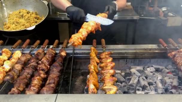 Brochetas giratorias o shashlik cocinar sobre carbones al aire libre en brochetas de metal. Carne marinada barbacoa cocinada al aire libre parrilla abierta en el patio de comidas en el mercado callejero. Primer plano. — Vídeo de stock