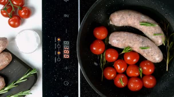 Salsicce bavaresi bianche grasse con pomodoro e rametto di rosmarino fritto in padella su fornello elettrico. Colazione all'inglese o tedesca, europea o americana. Vista dall'alto. Cibo dall'alto in basso. Primo piano. — Video Stock