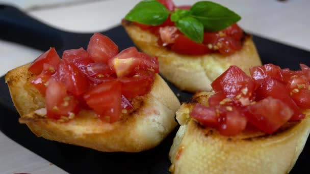 Chef preparando la clásica bruschetta italiana o mediterránea con baguette asado y espolvoreado con tomate. Decorado con hojas de albahaca. Snack vegetariano y vegano saludable. Primer plano. — Vídeo de stock