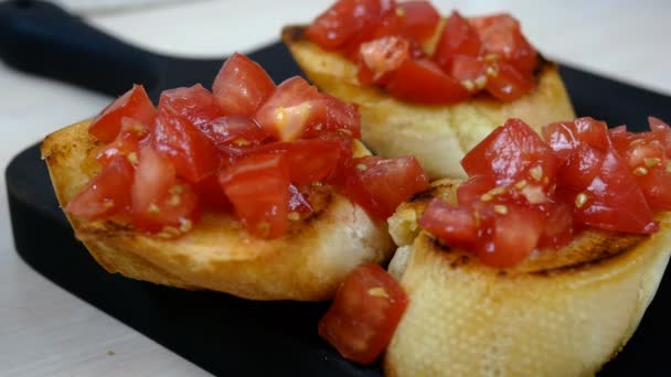 Šéfkuchař připravuje klasickou italskou nebo středomořskou bruschettu s pečenou bagetou a posypanou rajčaty. Zdobené listím bazalky. Zdravá veganská a vegetariánská svačinka. Detailní záběr. — Stock video