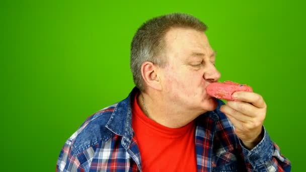 Senior adult caucasian ethnicity man savoring with pleasure eats cake with cream filling and drinks with pleasure milk from transparent glass with cocktail tube. Green screen. Chroma key. — Stock Video