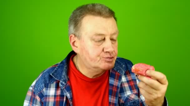 Senior adult caucasian ethnicity man greedily stuffs into mouth cake with cream filling, chew and licks his finger with pleasure. Green screen. Chroma key. Close-up. — Stock Video