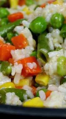 Geleneksel Meksika sebzeleri kızartılıyor. Mısır, kırmızı dolma biber, yeşil fasulye, yeşil bezelye, havuç, tavada pirinç karışımı. Tereyağı. Lezzetli vejetaryen yemek tarifi. Dikey çekim.