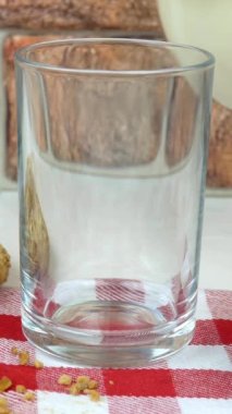 Taze doğal süt kafes peçetesindeki sürahiden bardağa dökülür. Yakınlarda reçel ve kurabiye var. Kahvaltıda bardağı sütle doldurmak. Dikey video.