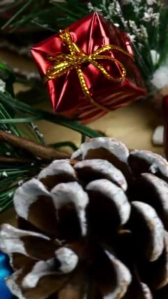 Decorações de Natal - ramos de abeto decorativos com bagas e cones, balas, presentes, flocos de neve giram no círculo no posto de madeira. Vídeo vertical. Fundo de Natal. — Vídeo de Stock