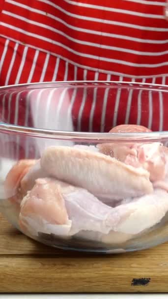 O chef prepara-se com asas de frango cruas de mãos para marinar. Adiciona sal, pimenta moída, páprica seca, molho de soja e misture em tigela de vidro transparente profundo. No balcão da cozinha. Vídeo vertical. — Vídeo de Stock