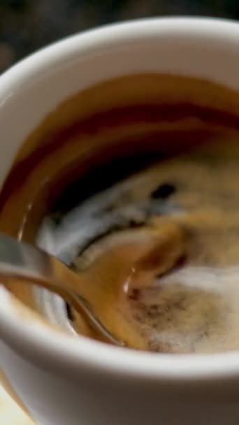 Café expreso caliente negro con espuma esponjosa se mezcla con cucharadita de metal en una taza de café blanco. Formato vertical. — Vídeo de stock