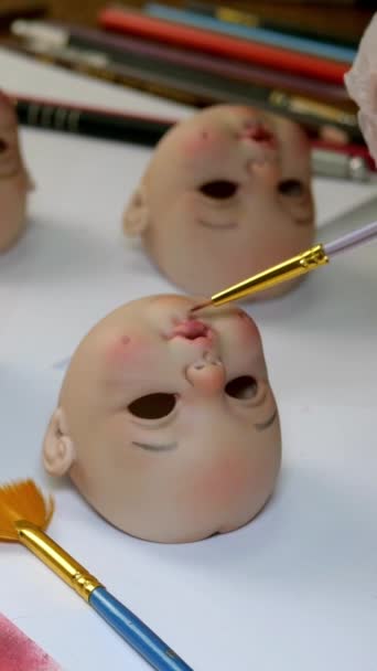 Making dolls. Master painter carefully paints lips of blank for doll with thin brush. Concept of combining work and hobbies. Vertical format. — Stock Video