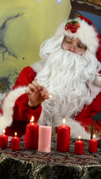 Jolly Santa acendeu velas enquanto estava sentado em uma árvore de Natal decorada com bolas de Natal e belas decorações e toca um sino e danças. Vídeo vertical. — Vídeo de Stock