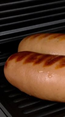 Kalın, yağlı sosisler elektrikli ızgarada kızartılır. Dikey video. Yakın plan..