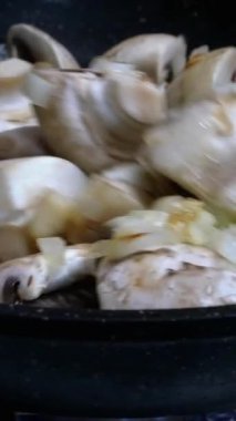 Çiğ, yenilebilir şampiyonlar, dört dilime bölünmüş soğanlar, kızartma tavasında karıştırılıp lezzetli yemekler yapıyorlar. Dikey video. Yakın plan..