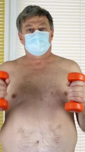 Mature adult Caucasian ethnic man runs on spot at home near window with blinds. Concept of fitness and health care on self-isolation during quarantine in elderly. Vertical video. — Stock Video