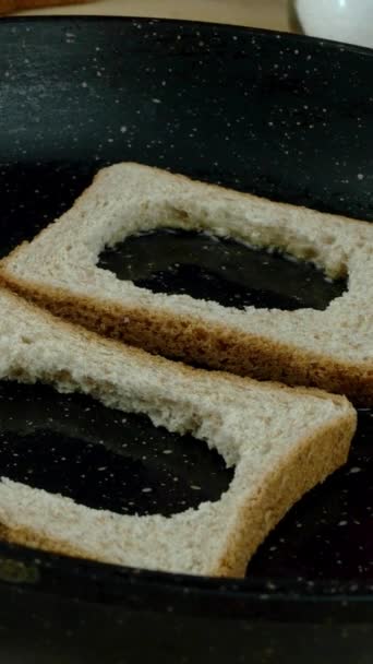 Bröd med hål placeras i pannan och ägg hälls i den och steks. Täck med lock. Smaklig stekt äggmacka recept. Hemkök. Vertikal video. Närbild. — Stockvideo