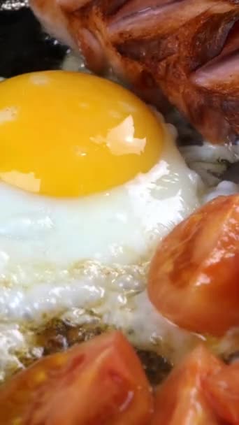 Rezept für ein schnelles leckeres traditionelles amerikanisches oder englisches Frühstück. Spiegeleier mit Würstchen und Tomaten in der Pfanne in der heimischen Küche zubereiten. Vertikales Video. — Stockvideo