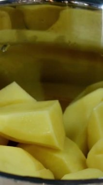 Şef büyük bir parça çiğ patatesi tencereye koyar ve patates püresi veya diğer yiyecekler için temiz soğuk suyla doldurur. Ev mutfağı tarifi. Dikey video. Yakın plan..