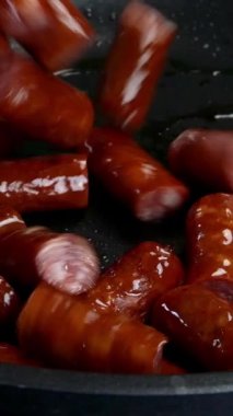 Lezzetli yağlı sosisler, parçalara ayrılmış, sebze yağında kızartma tavasında kızartılıyor. Hızlı besleyici yiyecekler. Ev mutfağı. Dikey video. Yakın plan..
