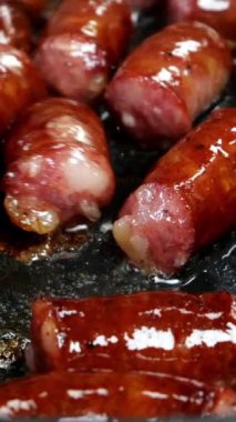 Lezzetli yağlı sosisler, parçalara ayrılmış, sebze yağında kızartma tavasında kızartılıyor. Hızlı besleyici yiyecekler. Ev mutfağı. Dikey video. Yakın plan..