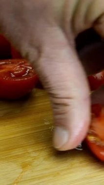 Şefin elleri lezzetli yemekler hazırlamak için kiraz domatesini ahşap kesme tahtasıyla keskin mutfak bıçağıyla parçalara ayırdı. Ev mutfağı. Dikey video. Yakın plan..