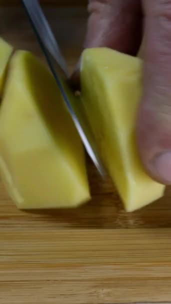 Chef sliced raw potatoes into large pieces with kitchen knife for making mashed potatoes or other food. On wooden cutting board. Home kitchen recipe. Vertical video. Close-up. — Stock Video