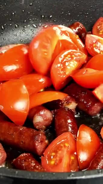 Deliciosas salsichas de caça gordurosas, cortadas em pedaços e tomate fatiado são fritas na frigideira em óleo vegetal. Comida nutritiva rápida. Cozinha caseira. Vídeo vertical. Close-up. — Vídeo de Stock